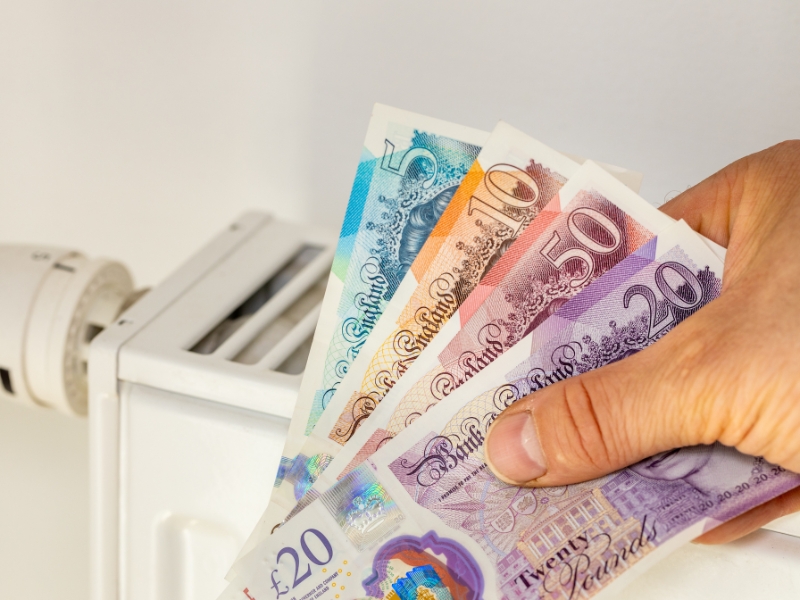 A hand holding british bank notes in front of a radiator