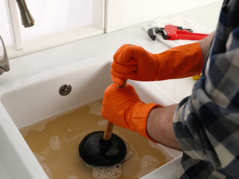 Someone unclogging a sink using a plunger