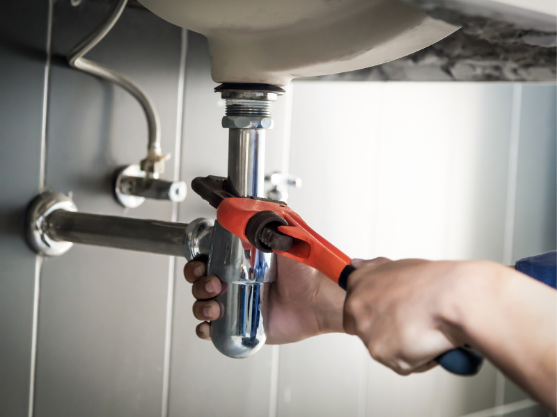 Close-up of a plumber using a wrench to tighten a pipe connection beneath a sink
