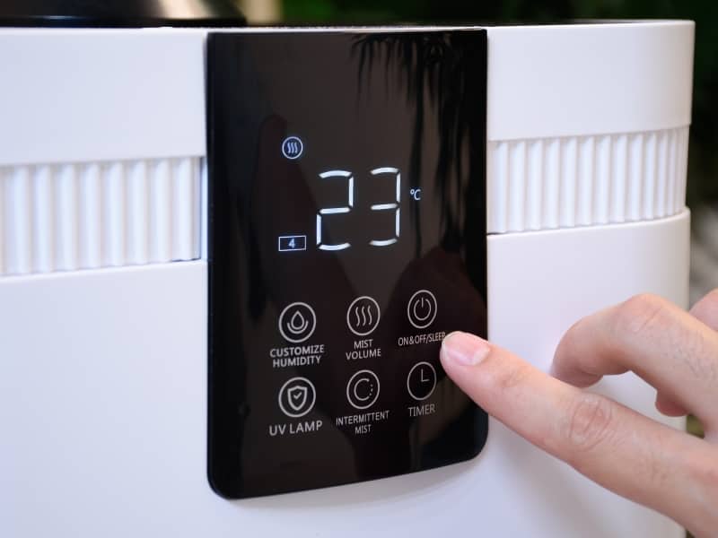 Close-up of a modern air conditioner display showing 23°C with a hand pressing the power button