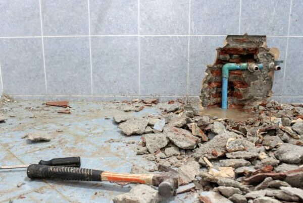 Damaged tiled wall with exposed water pipes and debris on the floor, indicating DIY plumbing work