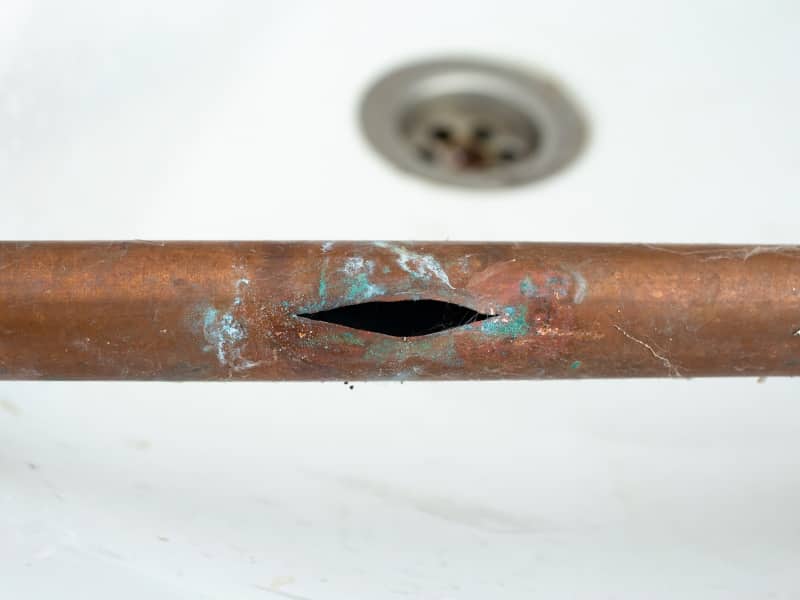 Close-up of a corroded copper pipe with a large split, showing signs of leakage and damage